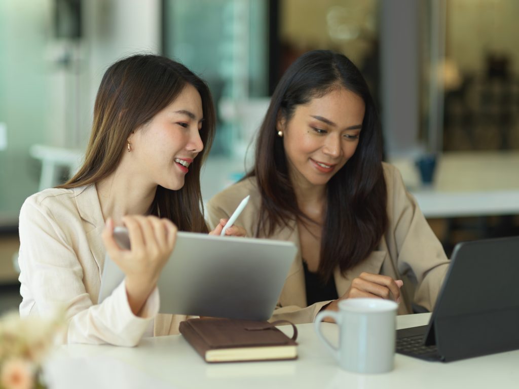 Two businesswomen talking to each other while working in office room